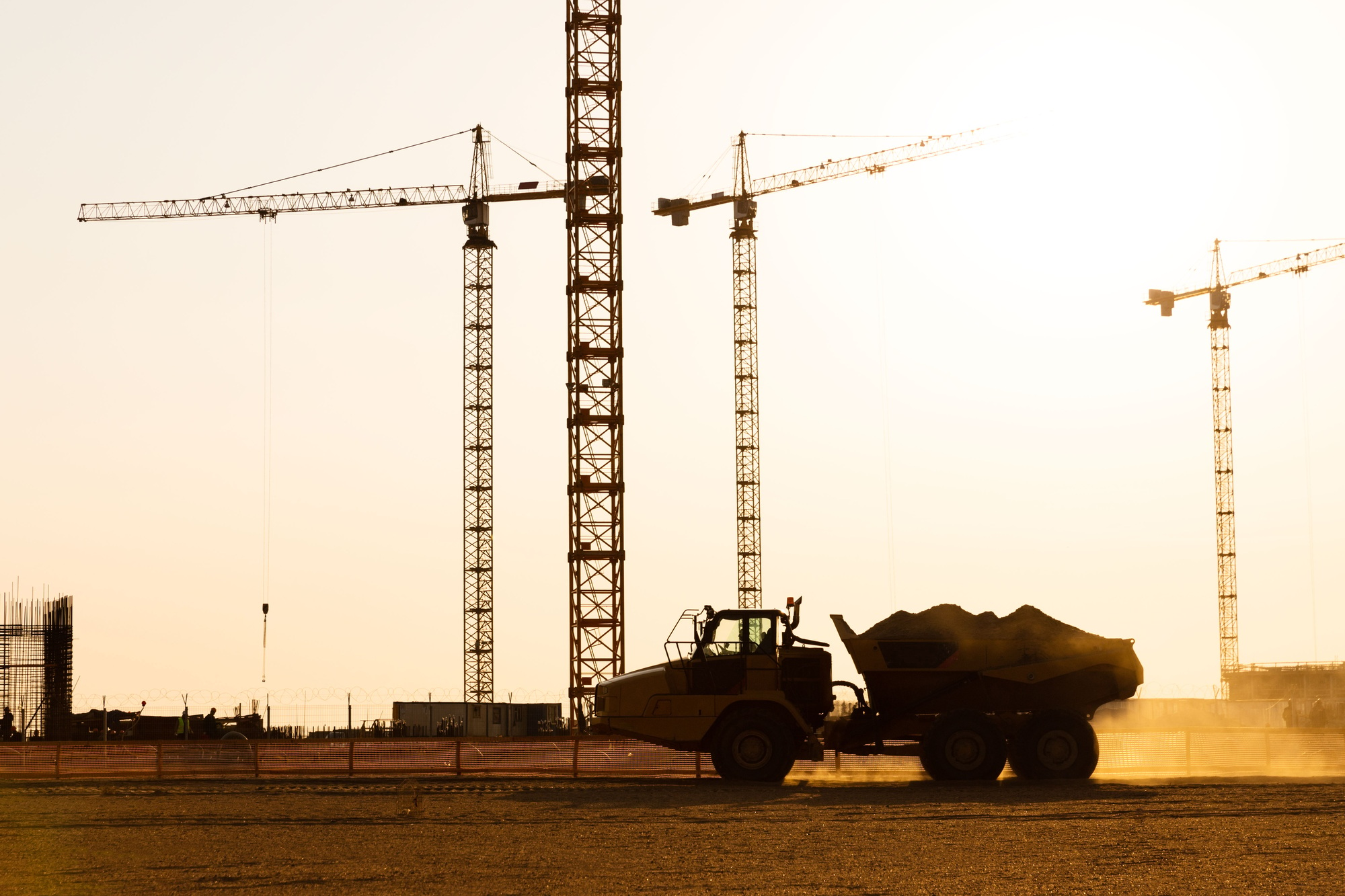 Group tower cranes and silhouette of dump truck at construction site, sunset sky background